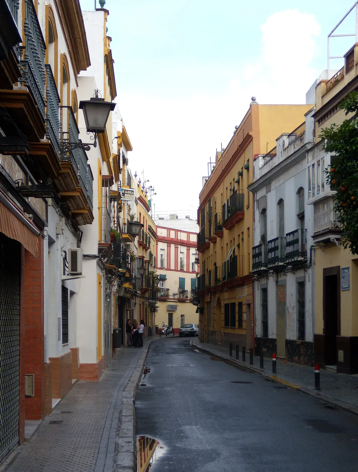 A narrow street in Triana lined with yellow and white houses and wrought-iron balconies
